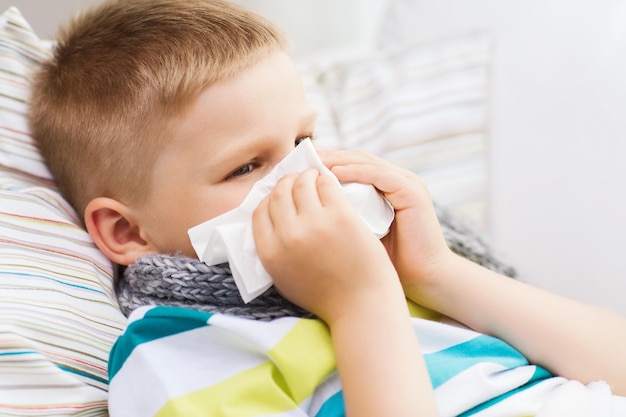 childhood, healthcare and medicine concept - ill boy with flu blowing nose at home