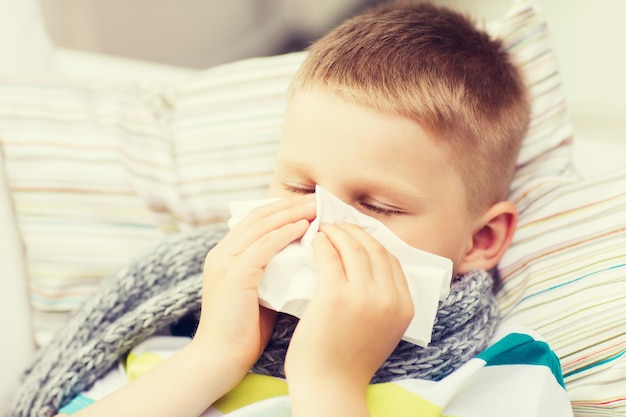 childhood, healthcare and medicine concept - ill boy with flu blowing nose at home