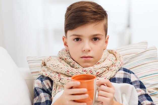 childhood, healthcare, people and medicine concept - ill boy with flu lying in bed and drinking tea at home