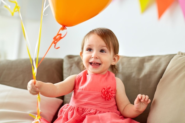 Photo childhood, holidays and people concept - happy baby girl with air balloons on birthday party at home