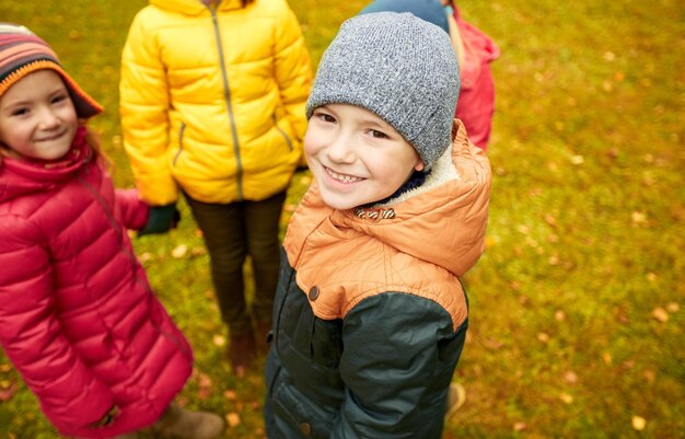 childhood, leisure, friendship and people concept - group of happy children holding hands and playing in autumn park