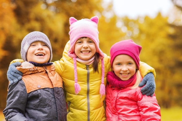 childhood, leisure, friendship and people concept - group of happy kids hugging in autumn park