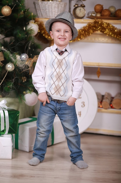 Foto ricordi d'infanzia. ragazzino con cappello festeggia il natale a casa. ragazzo bambino gioca vicino all'albero di natale. buon e luminoso natale. attività e gioco dell'infanzia. vacanza in famiglia.