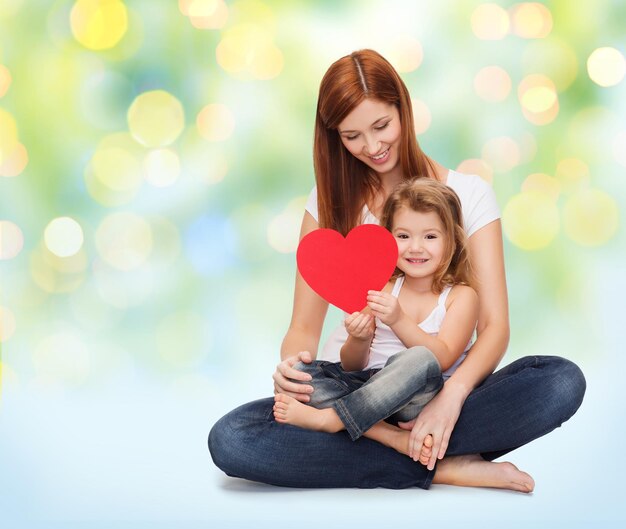 childhood, parenting, people and love concept - happy mother with adorable little girl holding red heart over green lights background