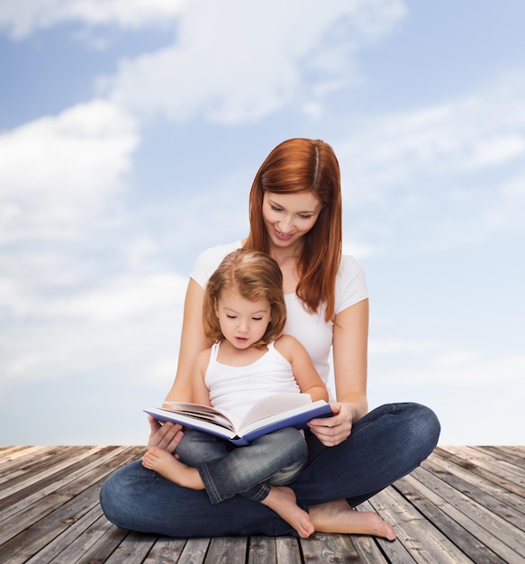 childhood, parenting and relationship concept - happy mother with adorable little girl reading book