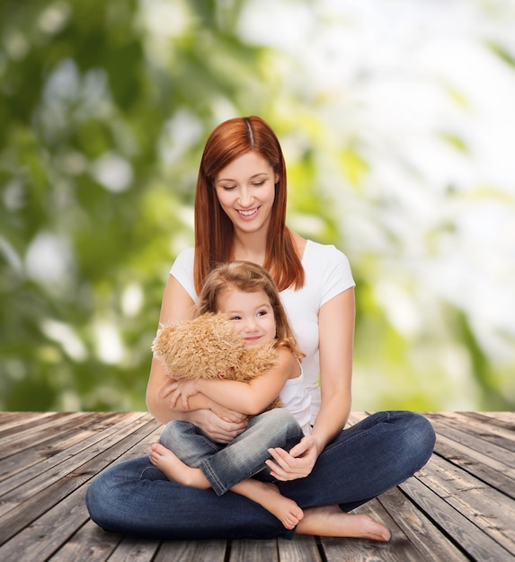 childhood, parenting and relationship concept - happy mother with adorable little girl and teddy bear