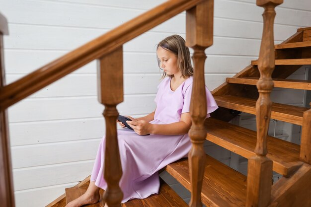 Childhood and people concept - beautiful smiling girl with tablet computer sitting on the stairs in the house