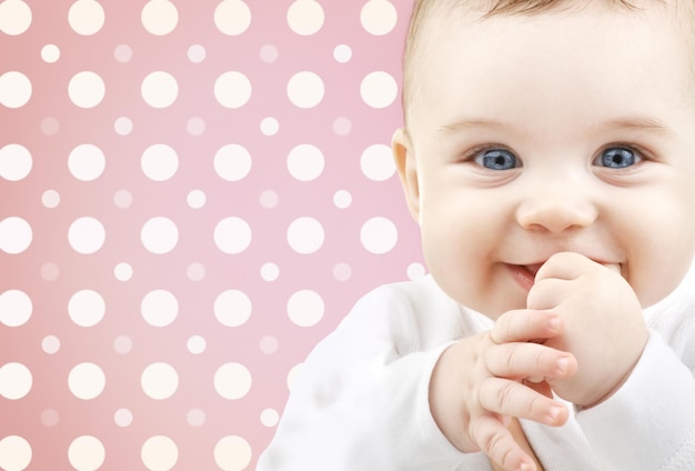 childhood, people and happiness concept - smiling baby girl face over pink and white polka dots pattern background