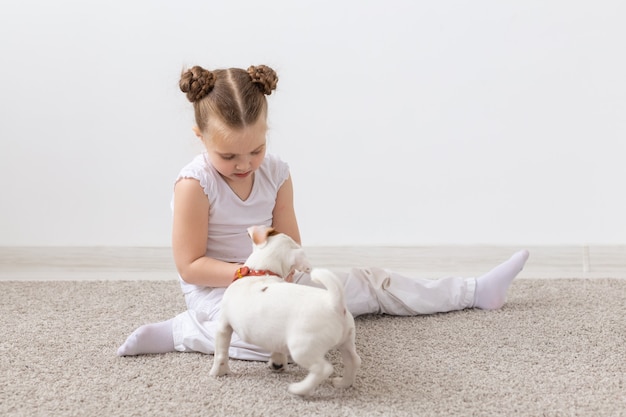 子供の頃、ペットと犬のコンセプト-楽しんでいる白いシャツの小さな子犬と子供の女の子。