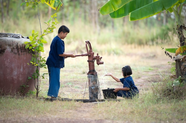 タイの田舎の子供時代小さな子供は水をバケツにポンプで注ぐことで家族を助けます