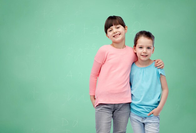 childhood, school, education, friendship and people concept - happy smiling little girls hugging over green chalk board background