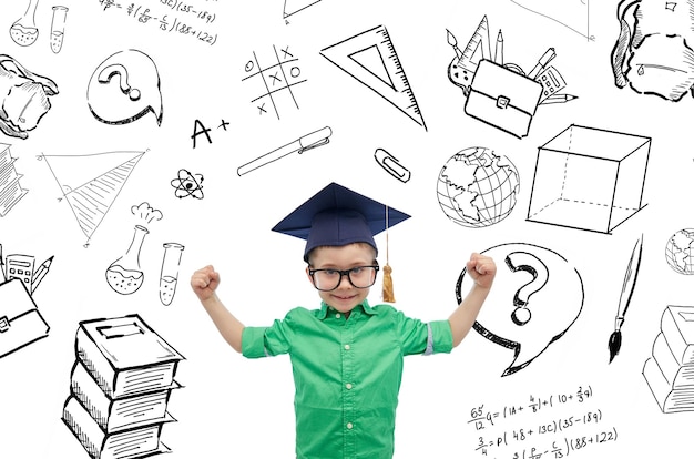 childhood, school, education, knowledge and people concept - happy boy in bachelor hat or mortarboard and eyeglasses showing strong hands with doodles