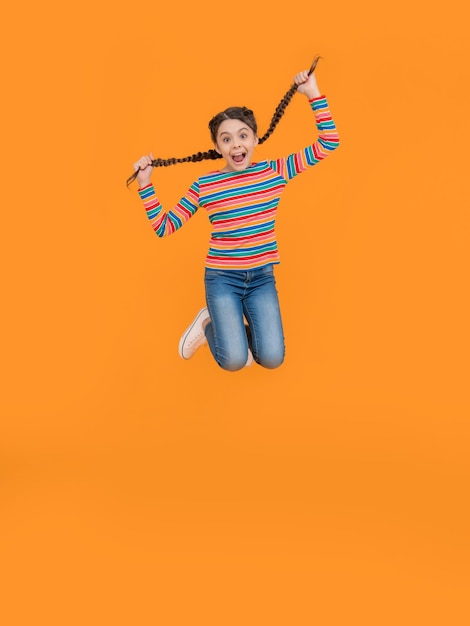 Childhood studio shot of jumping teen braided girl teen braided girl isolated on yellow background