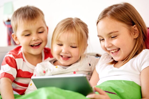 Photo childhood technology and family concept happy little kids with tablet pc computer in bed at home