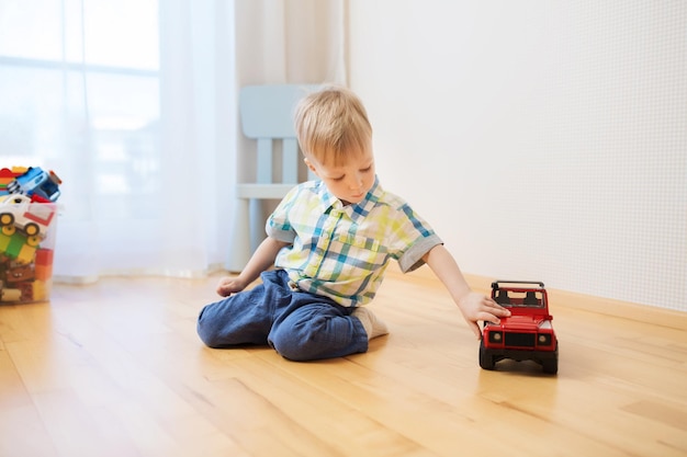 childhood, toys and people concept - little baby boy toy playing with car at home