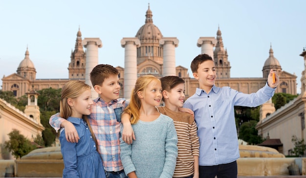 어린 시절, 여행, 관광, 기술 및 사람 개념 - 바르셀로나 국립 박물관 배경에서 스마트폰으로 셀카를 말하는 행복한 아이들