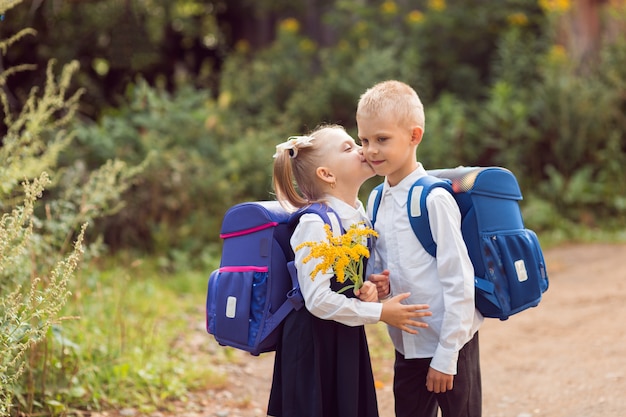 Фото Дети 7-8 лет, ученики начальной школы с рюкзаками и в школьной форме, девочка целует мальчика в щеку