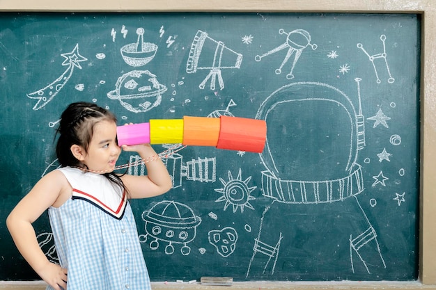 Children are learning science is interested universe system is stellar Holding a telescope made of paper xAThe background is a blackboard with a drawing