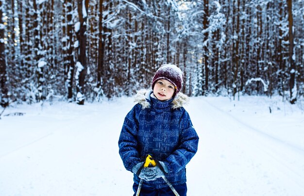 子供たちは雪に覆われた森の冬の日の健康的なライフスタイルでスキーをしています