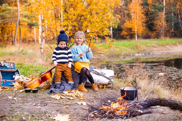 Bambini nella foresta di autunno su un picnic grigliano salsicce e suonano la chitarra