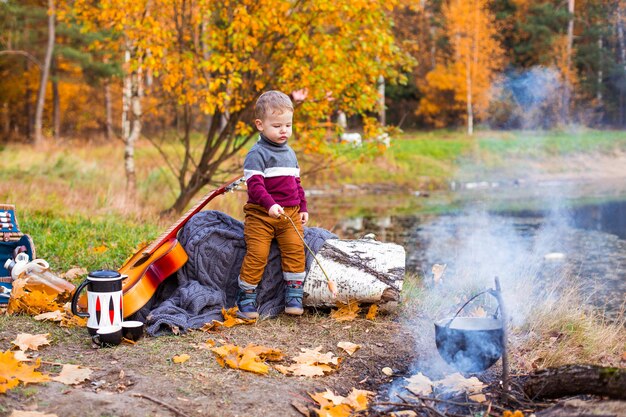 children in the autumn forest on a picnic grill sausages and play the guitar