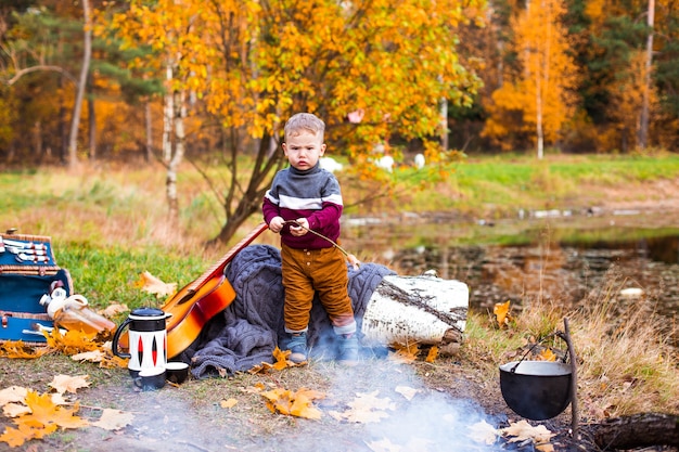 children in the autumn forest on a picnic grill sausages and play the guitar