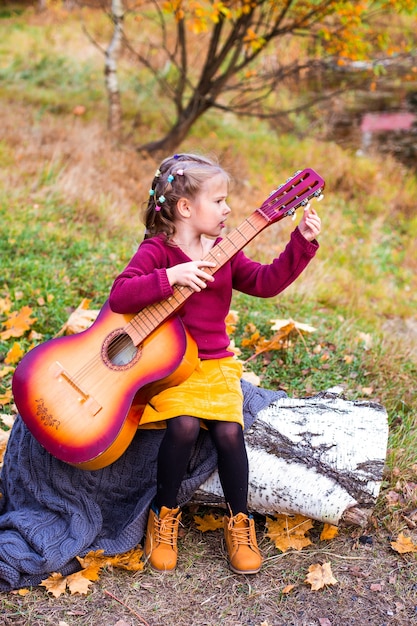 children in the autumn forest on a picnic play the guitar