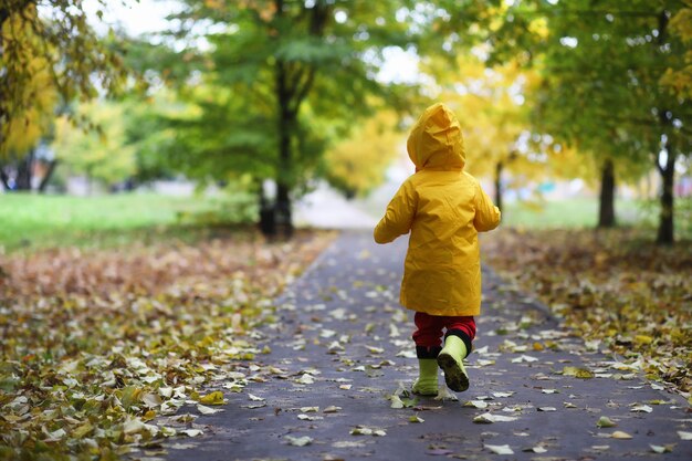 秋の公園の子供たちは日中レインコートを着て歩きます