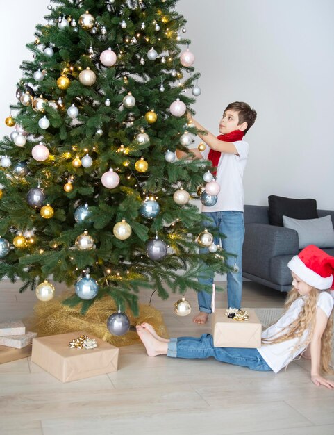 Дети - мальчик и девочка играют возле елки. Интерьер гостиной с елкой и украшениями. Новый год. Дарение подарков.