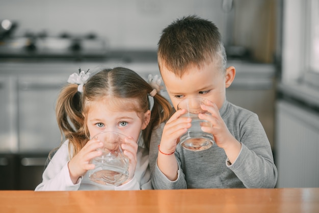 Foto bambini ragazzo e ragazza in cucina che bevono acqua dai bicchieri molto dolce