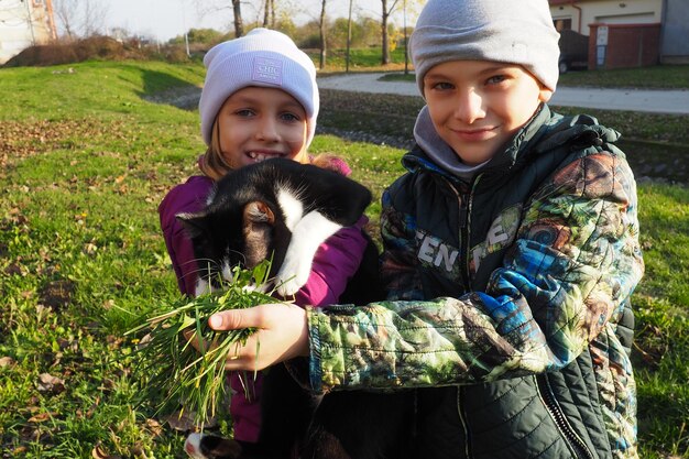 Children a boy and a girl of white race walk a black and white\
cat on the grassy lawn near the house the cat is afraid of a new\
place and tries to get out of hand autumn sunny day