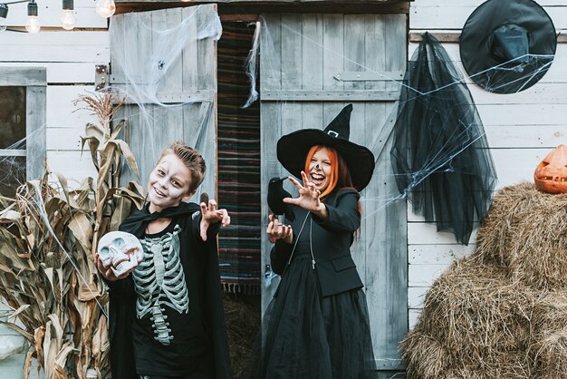 Bambini un ragazzo in costume da scheletro e una ragazza in costume da strega che si divertono a una festa di halloween sotto il portico decorato decorated