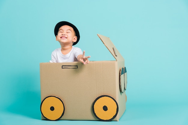 Sorriso del ragazzo dei bambini nella guida di un'auto da gioco creativa con l'immaginazione di una scatola di cartone