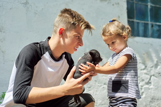 Children boy teenager and toddler girl with newborn black pig\
on farm.