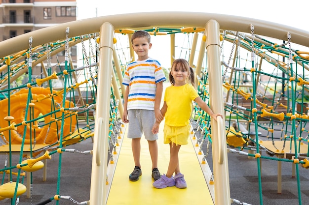 Children brother and sister play on a modern playground and climb a giant climbing web