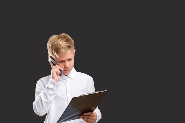 Children in business. Progressive generation. Smart boy working on project talking on phone isolated on gray.