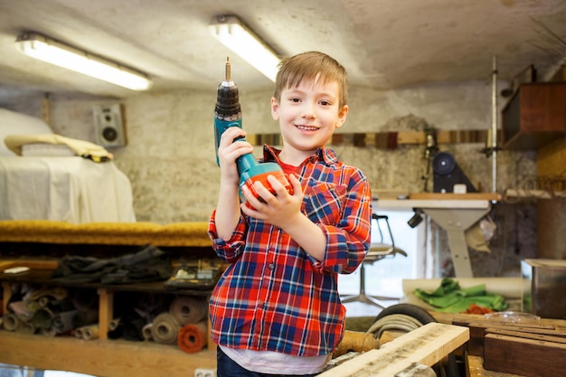 children, carpentry, profession and people concept - happy little boy with drill at workshop