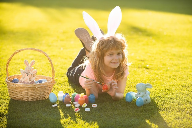 Children celebrating easter kid in rabbit costume with bunny ears painting eggs outdoor