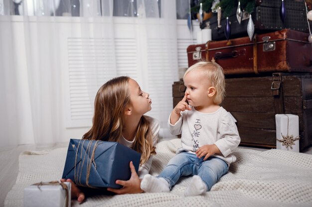 ギフトボックスとクリスマスツリーの下の子供たち。新年の飾り。素朴なスタイル、ダークウッドの装飾新年のインテリア。姉妹。