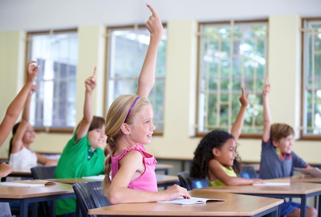 Foto bambini in classe e alzare le mani sul banco di scuola o bambini entusiasti che imparano per test e informazioni future conoscenza dell'istruzione e tabella per chiedere o rispondere all'esame o crescita e sviluppo del bambino