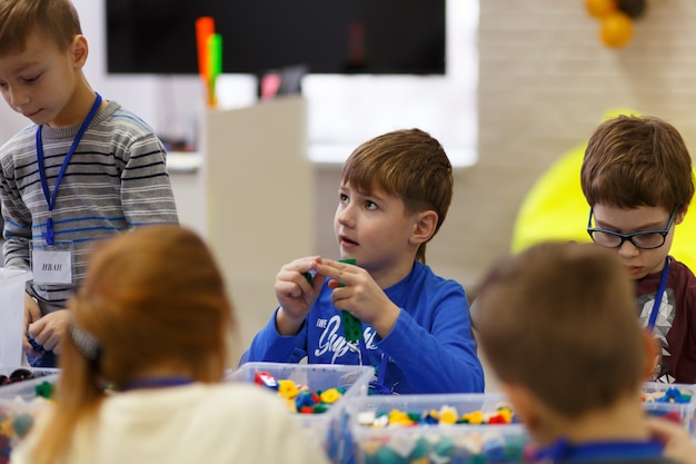 子供たちはデジタル技術の学校でコンストラクターのプラスチック部品からさまざまなオブジェクトを収集します