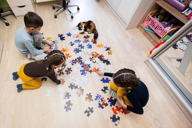 自宅の床の子供部屋でジグソー パズルのピースをつなぐ子供たち 楽しい家族活動レジャー