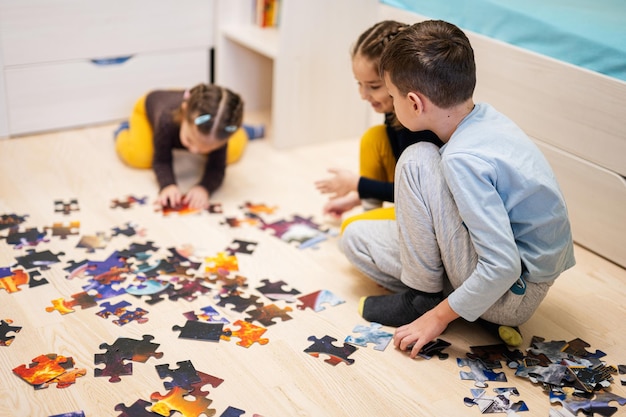 自宅の床の子供部屋でジグソー パズルのピースをつなぐ子供たち 楽しい家族活動レジャー