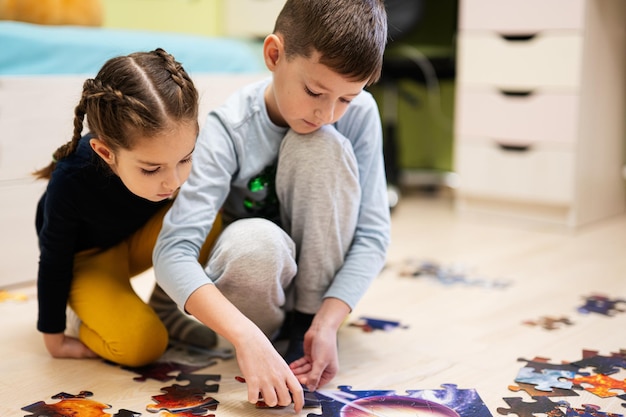 自宅の床の子供部屋でジグソー パズルのピースをつなぐ子供たち 楽しい家族活動レジャー