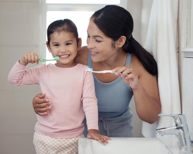 Children dental and toothbrush with a girl and her mother\
brushing their teeth together in the bathroom of their home family\
hygiene and oral with a woman and daughter practicing care and\
hygiene