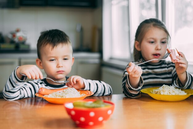 Children eat pasta and sausage in the kitchen