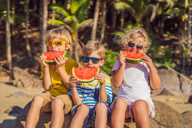 Children eat watermelon on the beach in sunglasses