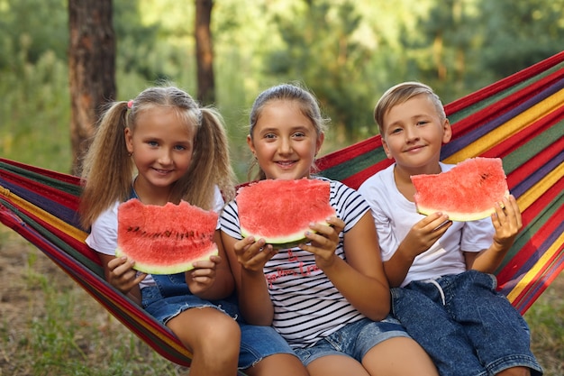 Children eat watermelon and joke, in the fresh air, sitting on a hammock