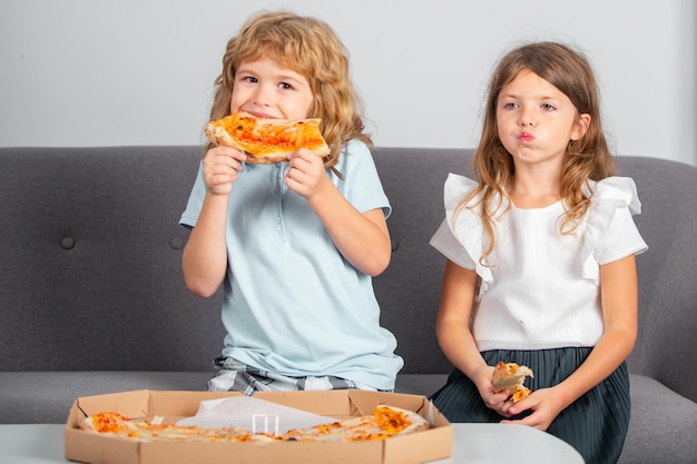 Children eating pizza two young children bite pizza indoors