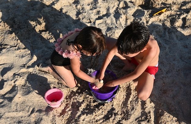 ビーチで砂のフィギュアの建設を楽しんでいる子供たち男の子と女の子がおもちゃのプラスチック製のバックを埋めます